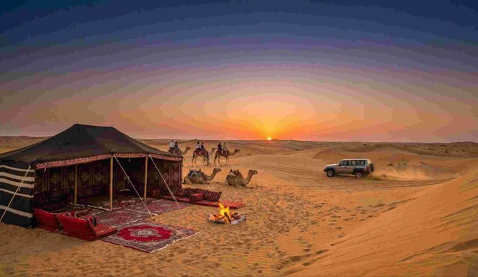 A desert campsite with a Bedouin tent, campfire, camels, and a 4x4 vehicle during a beautiful sunset, showcasing the perfect conditions that make it the Best time to visit Jeddah desert.