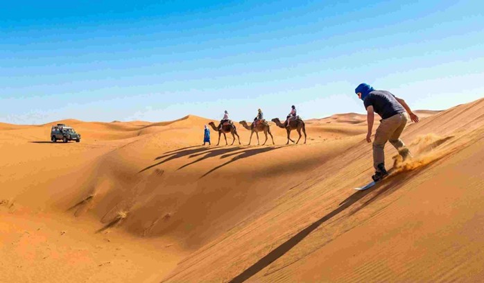 A thrilling photo of a white Toyota Land Cruiser 4x4 kicking up sand as it speeds over a steep desert dune, with the Red Sea coast visible in the background, depicting Dune bashing in Jeddah.