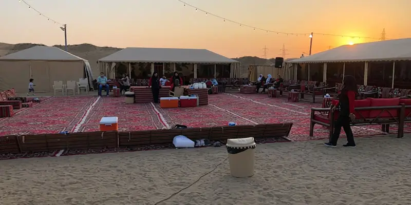 Traditional desert camp layout with red carpets and Bedouin tents set up on the sand at sunset near Jeddah.