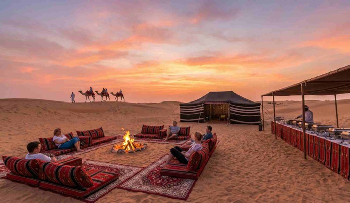 A group of people relax around a campfire and enjoy a buffet dinner at a desert camp during a stunning sunset, illustrating the relaxing atmosphere of an evening tour when comparing a Morning vs evening desert safari Jeddah.