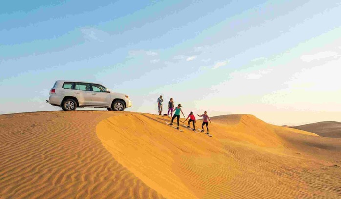 A bright and sunny desert laandscape with a 4x4 vehicle driving over golden dunes under a clear blue sky, showcasing the daytime adventure option when comparing a Morning vs evening desert safari Jeddah.