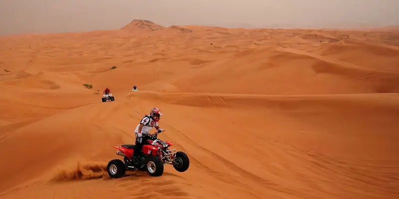 Quad bike rider speeding over vast sand dunes during an off-road adventure in the Jeddah desert.