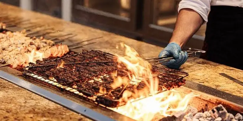 Chef grilling fresh meat skewers over open flames at a live BBQ station during a desert camp dinner near Jeddah.