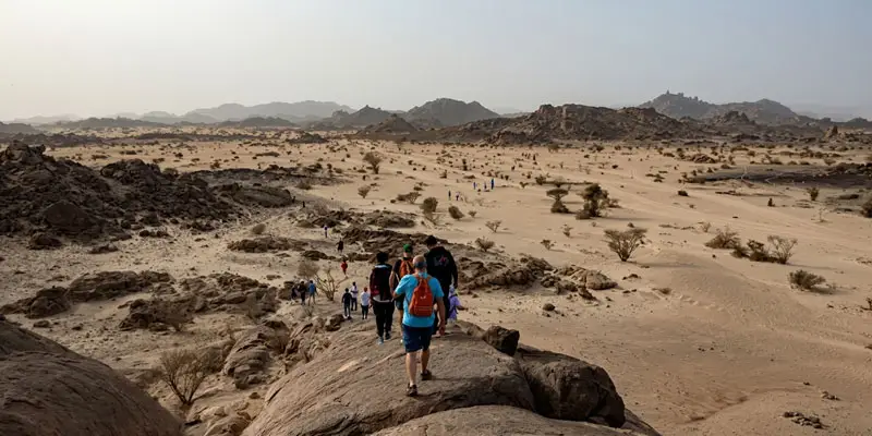 Group of hikers trekking along giant rock formations overlooking the desert landscape in Moon Valley, Jeddah.