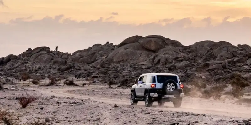 White FJ Cruiser driving on a dirt road toward granite rock formations in Moon Valley, Jeddah.
