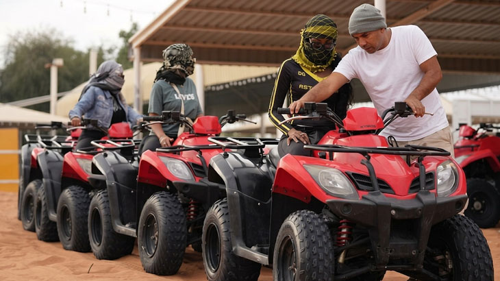 Riders and instructors preparing red quad bikes under a shelter before a desert adventure in Jeddah.